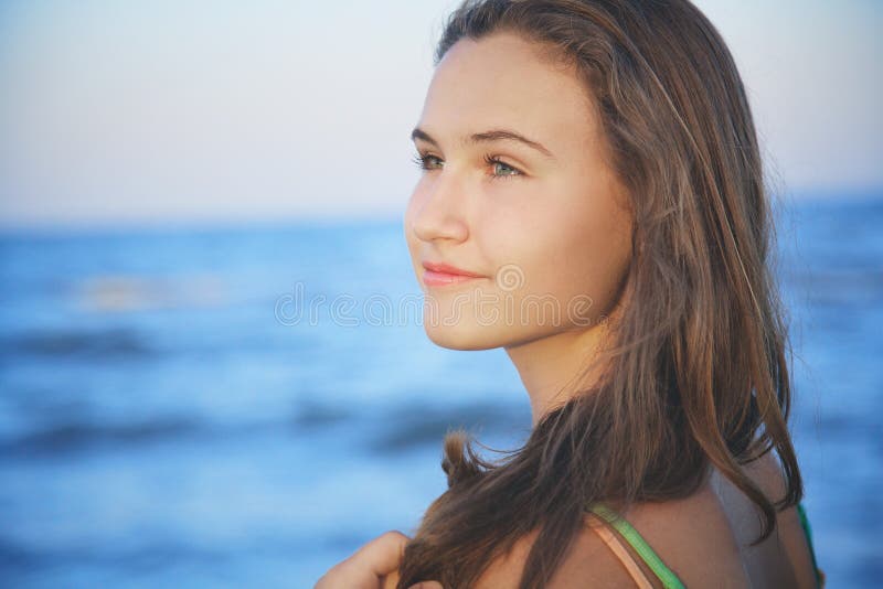 Brown-haired young romantic teenager girl corrects long hair on beach at summer evening wind. Brown-haired young romantic teenager girl corrects long hair on beach at summer evening wind