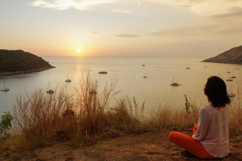 A moça que senta-se na posição da meditação dos lótus da ioga na parte dianteira ao beira-mar sobre as rochas uma observação do s foto de stock royalty free A moça que senta-se na posição da meditação dos lótus da ioga na parte dianteira ao beira-mar sobre as rochas uma observação do s foto de stock royalty free