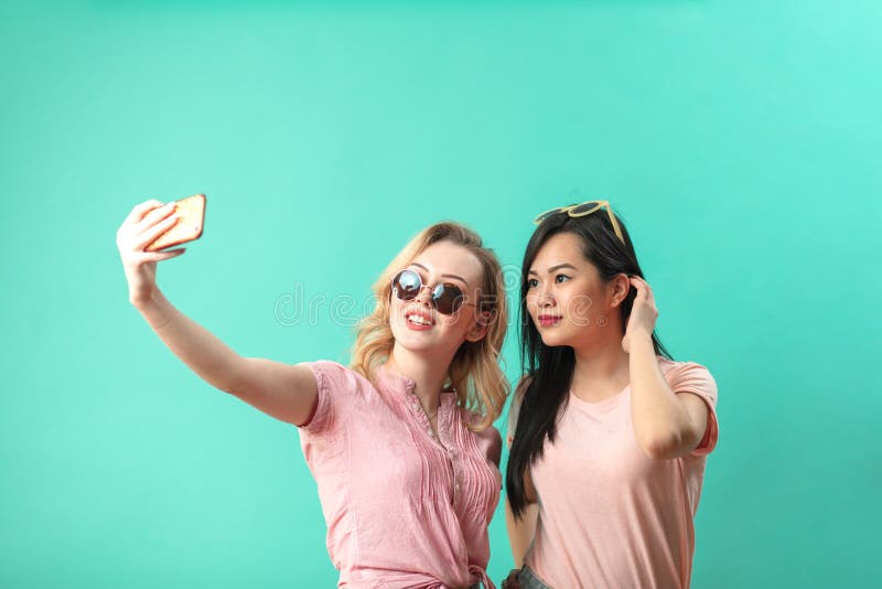 Moças diversas felizes que tomam o selfie com o smartphone contra a parede azul fotos de stock royalty free Moças diversas felizes que tomam o selfie com o smartphone contra a parede azul fotos de stock royalty free