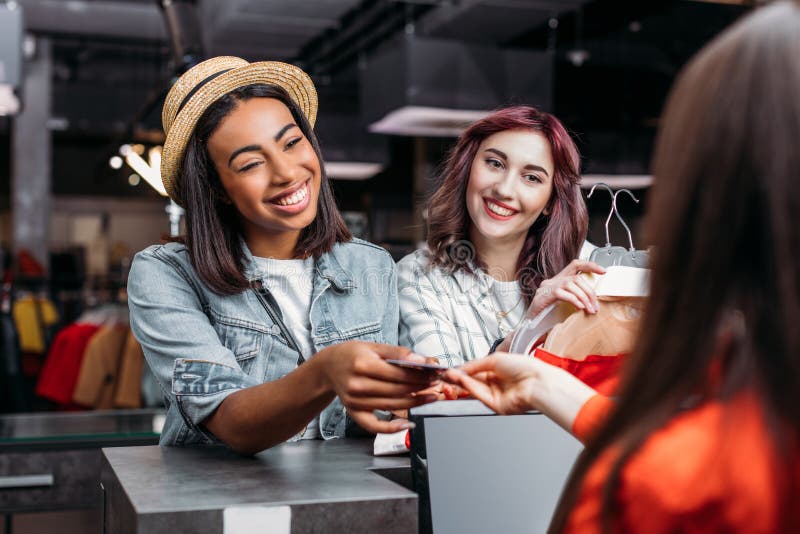 Moças multiculturais que compram e que pagam com o cartão de crédito no boutique fotos de stock Moças multiculturais que compram e que pagam com o cartão de crédito no boutique fotos de stock