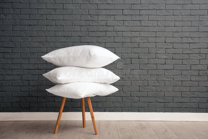 Mucchio dei cuscini di letto molli sulla sedia vicino al muro di mattoni
