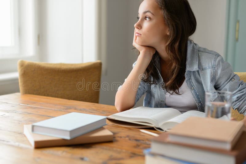 Muchacha aburrida del estudiante que sienta a casa la mirada lejos foto de archivo