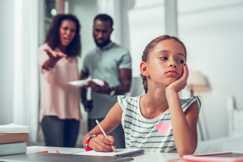 Muchacha aburrida que estudia mientras que sus padres que discuten su mún académico imagen de archivo libre de regalías Muchacha aburrida que estudia mientras que sus padres que discuten su mún académico imagen de archivo libre de regalías