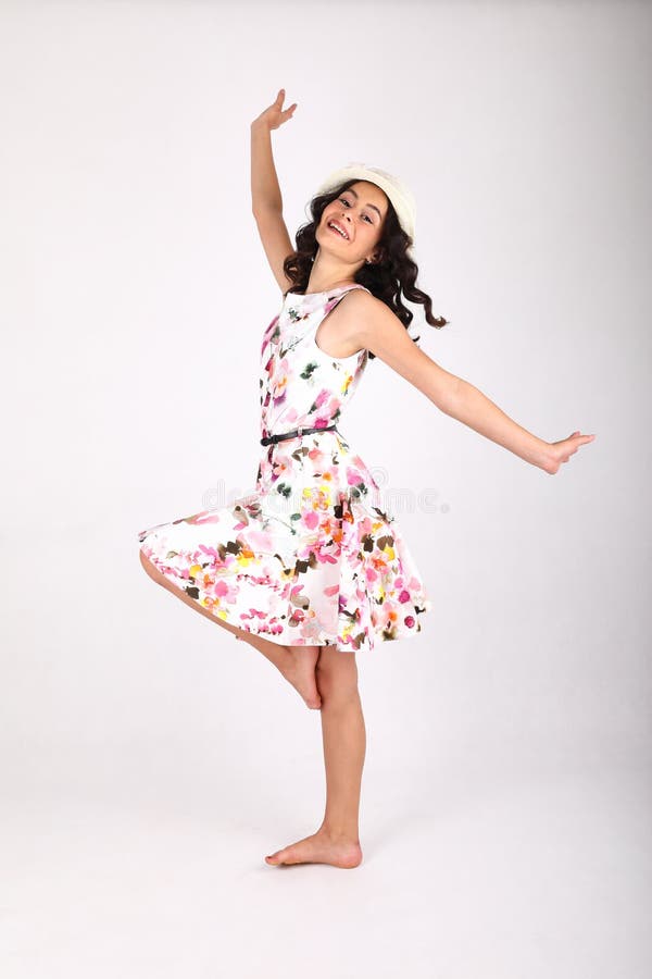 Pretty teenage girl - happy smiling barefoot schoolkid with brunette hair dressed in nice light summer dress and white hat dancing on white background. Portrait photography concept. Pretty teenage girl - happy smiling barefoot schoolkid with brunette hair dressed in nice light summer dress and white hat dancing on white background. Portrait photography concept.