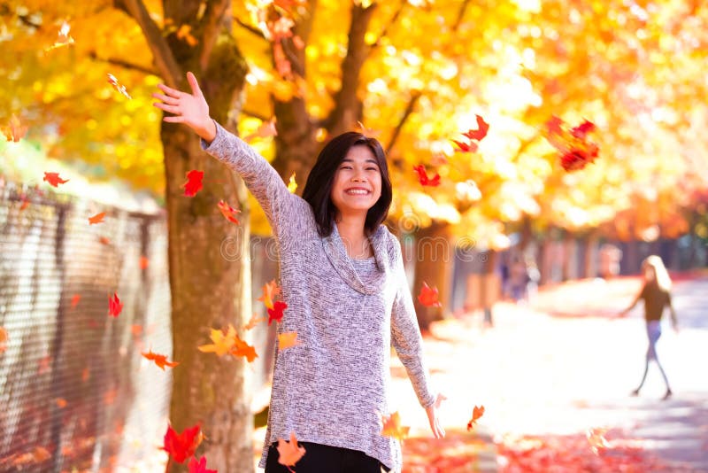 Muchacha adolescente que lanza las hojas de otoño coloridas en aire debajo de árboles imágenes de archivo libres de regalías Muchacha adolescente que lanza las hojas de otoño coloridas en aire debajo de árboles imágenes de archivo libres de regalías