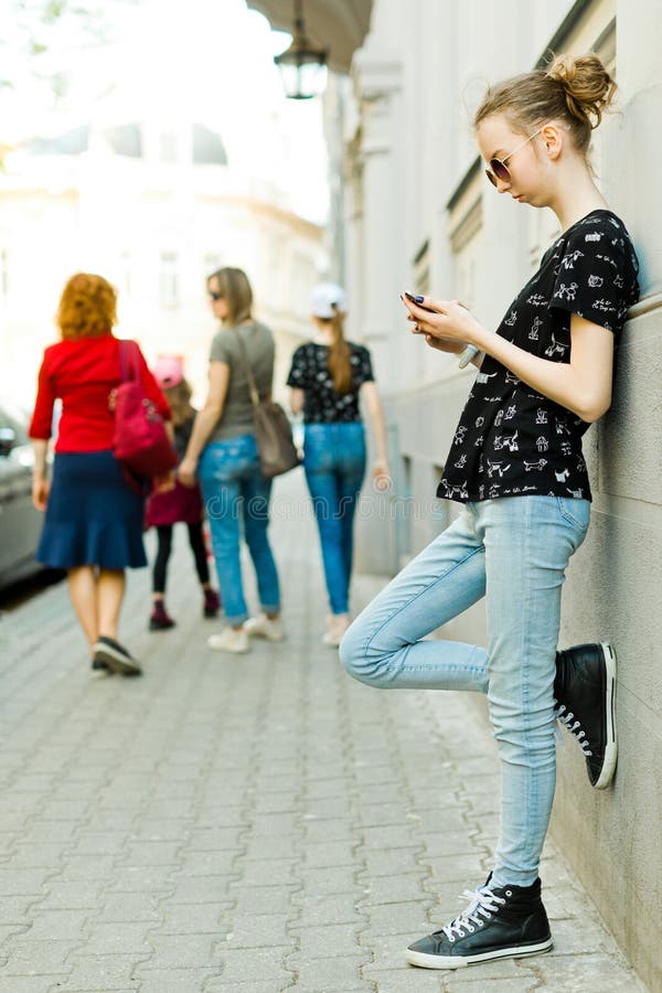 Muchacha adolescente que se inclina contra la pared y que usa el teléfono celular imagen de archivo Muchacha adolescente que se inclina contra la pared y que usa el teléfono celular imagen de archivo