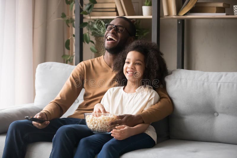 Muchacha afroamericana alegre TV de observación de risa del padre y del niño fotografía de archivo