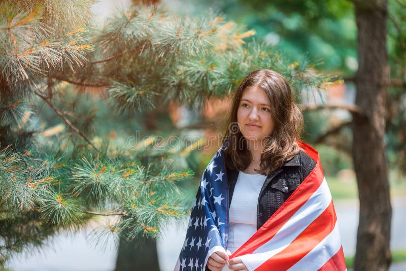 Muchacha americana sonriente que celebra la bandera y la mirada de los E.E.U.U. de D?a de la Independencia de la c?mara imagen de archivo libre de regalías Muchacha americana sonriente que celebra la bandera y la mirada de los E.E.U.U. de D?a de la Independencia de la c?mara imagen de archivo libre de regalías