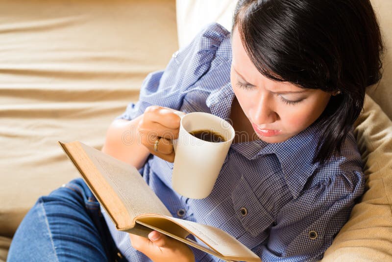 Student - Young asian woman or girl sitting on a sofa with a cup of coffee reading a book, she is learning. Student - Young asian woman or girl sitting on a sofa with a cup of coffee reading a book, she is learning
