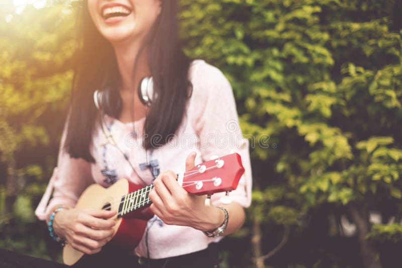 Muchacha asiática feliz que juega el ukelele en al aire libre fotos de archivo Muchacha asiática feliz que juega el ukelele en al aire libre fotos de archivo