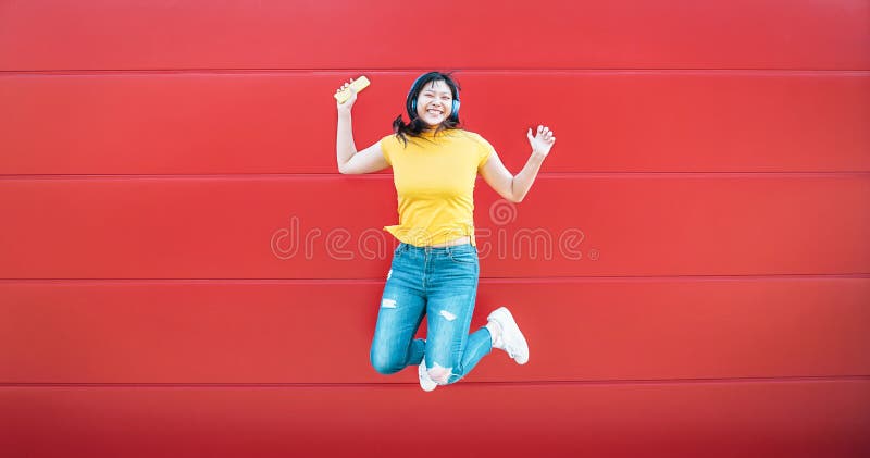 Muchacha asiática feliz que salta mientras que música que escucha al aire libre - mujer china loca que se divierte que baila una fotos de archivo Muchacha asiática feliz que salta mientras que música que escucha al aire libre - mujer china loca que se divierte que baila una fotos de archivo
