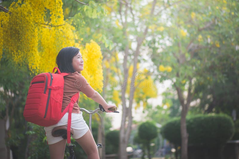 Muchacha asiática hermosa con la bicicleta roja del montar a caballo de la mochila en el parque fotografía de archivo Muchacha asiática hermosa con la bicicleta roja del montar a caballo de la mochila en el parque fotografía de archivo