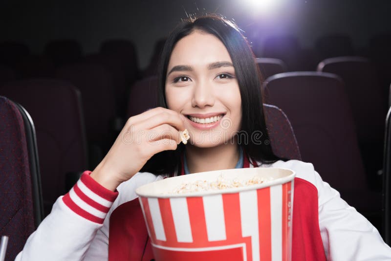 Muchacha asiática joven que come las palomitas y que mira película fotografía de archivo
