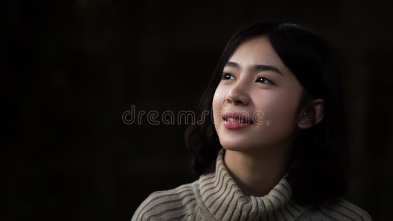 Muchacha asiática que mira para arriba en el fondo oscuro imagen de archivo Muchacha asiática que mira para arriba en el fondo oscuro imagen de archivo