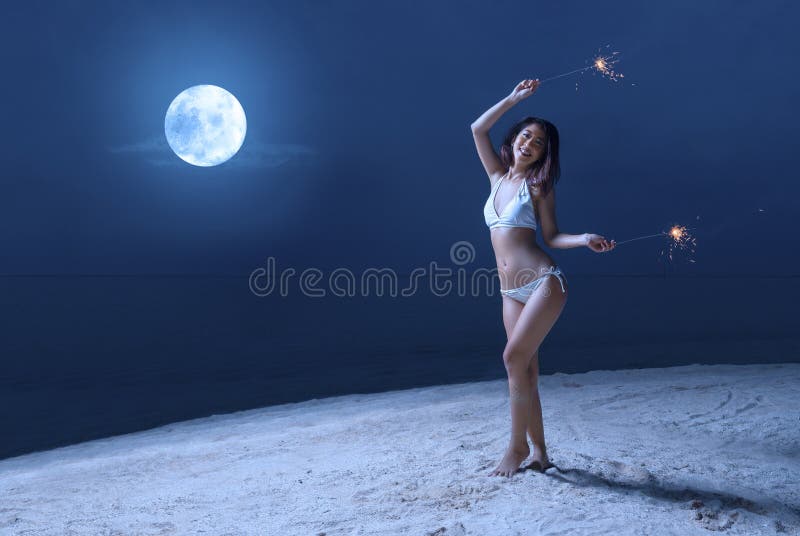 Muchacha atractiva asi?tica en el bikini que sostiene los fuegos artificiales en la playa en la noche imagenes de archivo Muchacha atractiva asi?tica en el bikini que sostiene los fuegos artificiales en la playa en la noche imagenes de archivo
