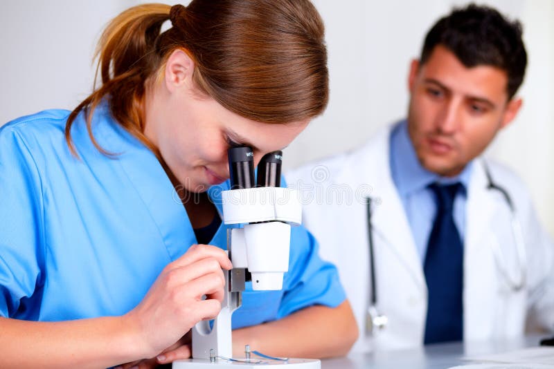Muchacha bastante caucásica del doctor que usa un microscopio fotografía de archivo libre de regalías Muchacha bastante caucásica del doctor que usa un microscopio fotografía de archivo libre de regalías