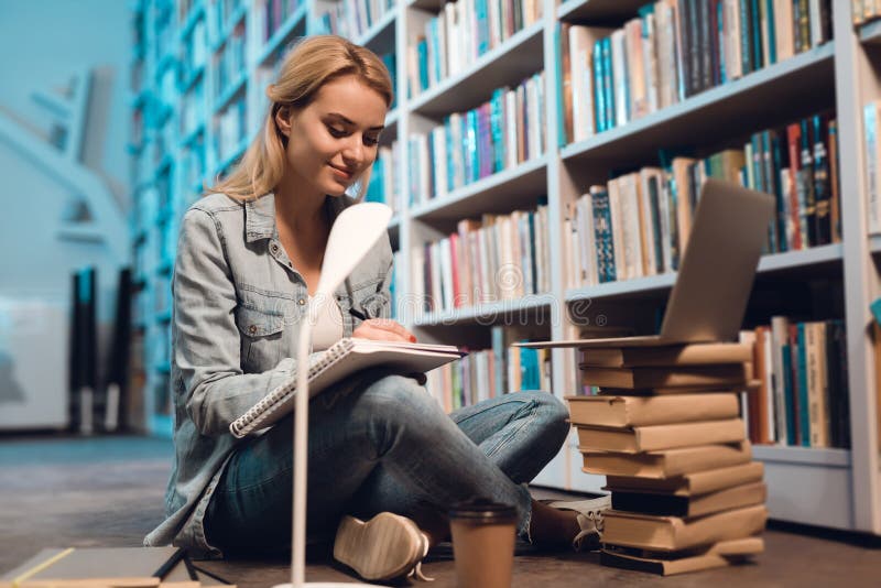 Muchacha blanca cerca del estante en biblioteca El estudiante está tomando notas fotos de archivo libres de regalías Muchacha blanca cerca del estante en biblioteca El estudiante está tomando notas fotos de archivo libres de regalías