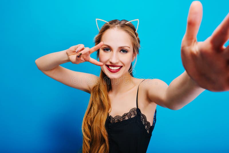 Muchacha bonita alegre con los oídos de gato en diamantes en la cabeza que presenta a la cámara, tomando el selfie, mostrando la fotos de archivo Muchacha bonita alegre con los oídos de gato en diamantes en la cabeza que presenta a la cámara, tomando el selfie, mostrando la fotos de archivo