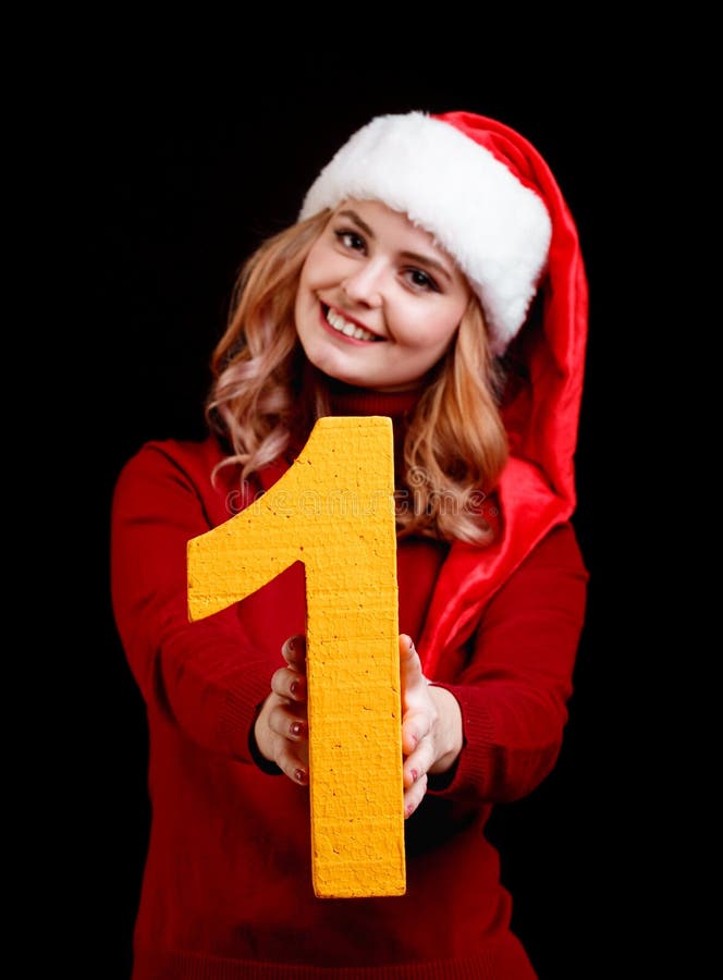 Muchacha bonita sonriente en un sombrero de la Navidad que lleva a cabo el número 1 en un fondo negro Concepto 2018 del Año Nuevo imagen de archivo libre de regalías Muchacha bonita sonriente en un sombrero de la Navidad que lleva a cabo el número 1 en un fondo negro Concepto 2018 del Año Nuevo imagen de archivo libre de regalías