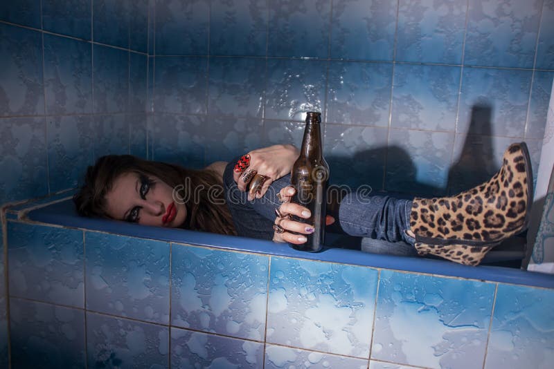 Muchacha borracha que miente en una bañera con una botella en su mano foto de archivo libre de regalías Muchacha borracha que miente en una bañera con una botella en su mano foto de archivo libre de regalías