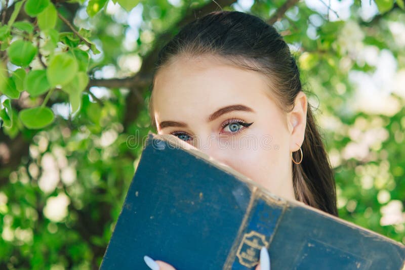 Girl in a white blouse and blue jeans. Stands near a flowering tree and reads a book. Girl in a white blouse and blue jeans. Stands near a flowering tree and reads a book.