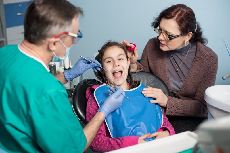Muchacha con la madre en la primera visita dental Dentista de sexo masculino mayor que hace el primer chequeo para el paciente en fotografía de archivo libre de regalías Muchacha con la madre en la primera visita dental Dentista de sexo masculino mayor que hace el primer chequeo para el paciente en fotografía de archivo libre de regalías