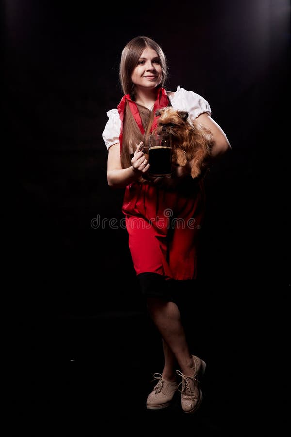 Muchacha con ropa étnica nacional con perro pequeño en la mano posando en un estudio de fondo negro. una joven con un vestido rojo foto de archivo libre de regalías