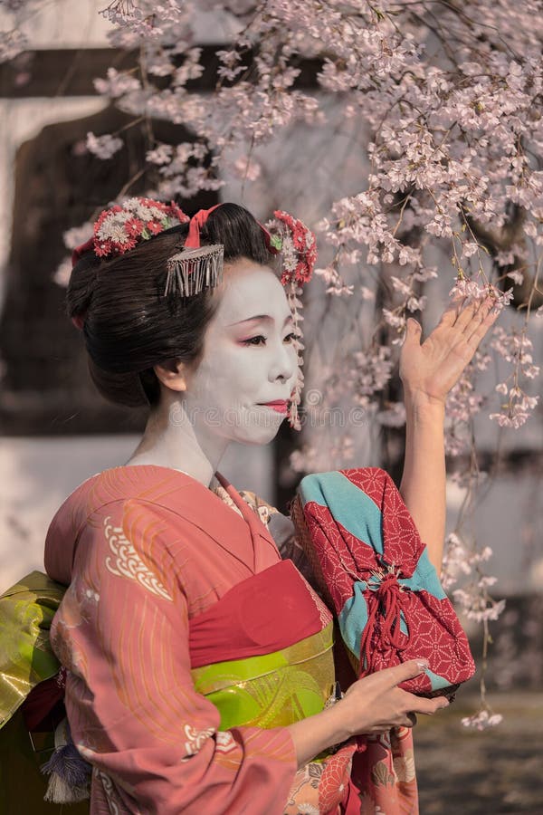 Muchacha de geisha en un kimono que presenta delante de un hous japonés tradicional imagen de archivo Muchacha de geisha en un kimono que presenta delante de un hous japonés tradicional imagen de archivo