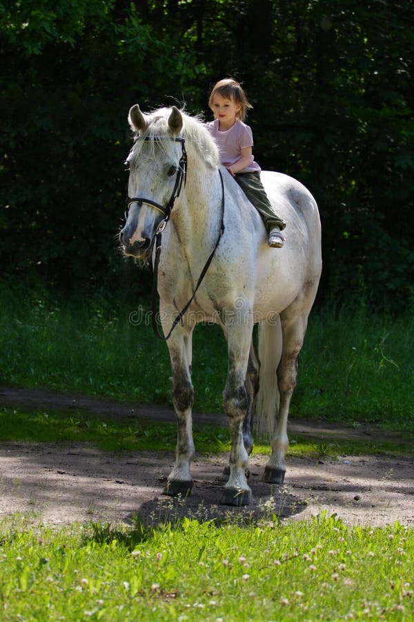 Little beauty satisfied girl riding bareback by gray beautiful big horse with black bridle. Little beauty satisfied girl riding bareback by gray beautiful big horse with black bridle.