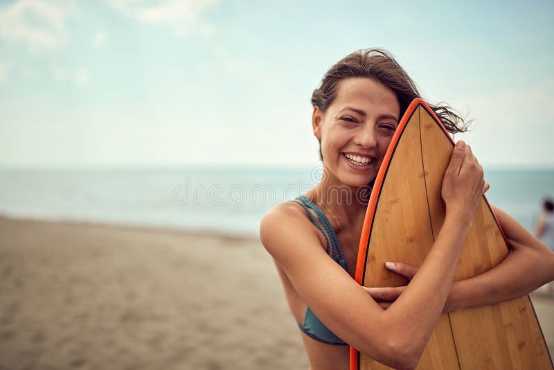 Muchacha de la persona que practica surf que presenta con su tabla hawaiana en la playa