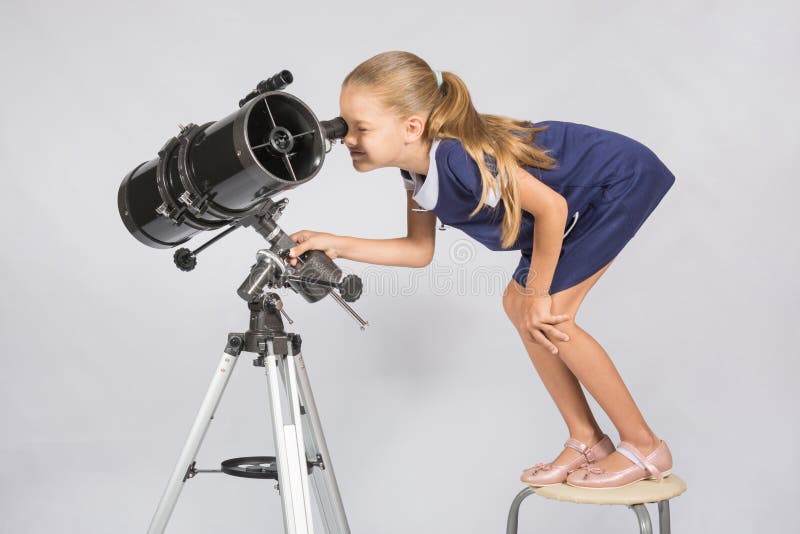Muchacha de siete años que se coloca en una silla y las miradas ridículas en el ocular del reflector del telescopio foto de archivo libre de regalías Muchacha de siete años que se coloca en una silla y las miradas ridículas en el ocular del reflector del telescopio foto de archivo libre de regalías