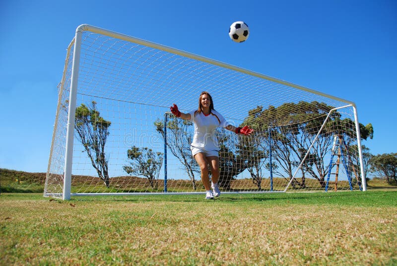 A beautiful active caucasian white female goalkeeper standing in the goal trying to catch the soccer ball on the field outdoors. A beautiful active caucasian white female goalkeeper standing in the goal trying to catch the soccer ball on the field outdoors