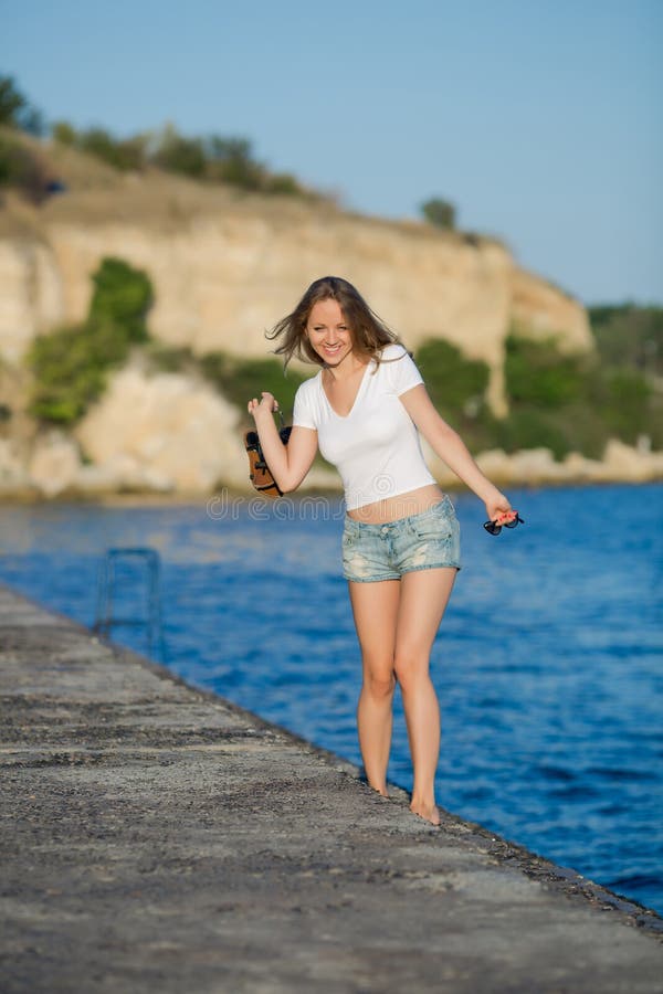 Muchacha descalza en pantalones cortos que camina en el muelle concreto mojado fotografía de archivo libre de regalías Muchacha descalza en pantalones cortos que camina en el muelle concreto mojado fotografía de archivo libre de regalías