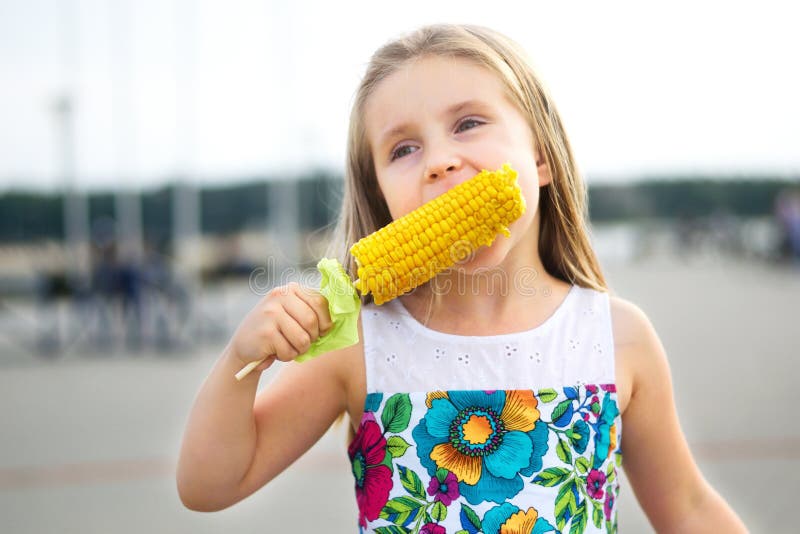 Muchacha divertida adorable que come el maíz en la mazorca en día de verano soleado