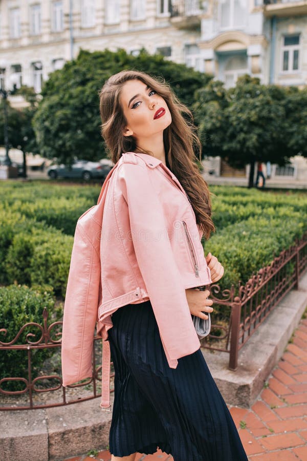 Muchacha elegante con el pelo rizado largo que presenta en buey en fondo de la yarda Ella lleva el vestido negro, chaqueta rosada imágenes de archivo libres de regalías Muchacha elegante con el pelo rizado largo que presenta en buey en fondo de la yarda Ella lleva el vestido negro, chaqueta rosada imágenes de archivo libres de regalías