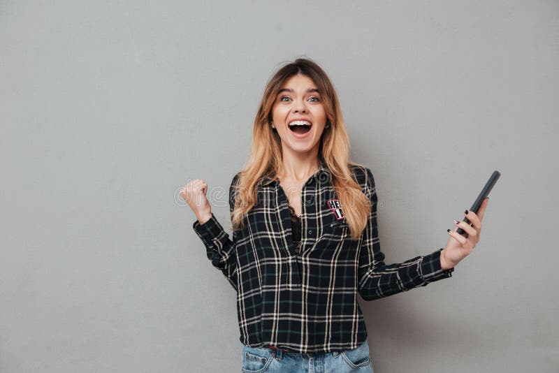 Muchacha emocionada feliz que sostiene el teléfono móvil y que celebra triunfo foto de archivo libre de regalías