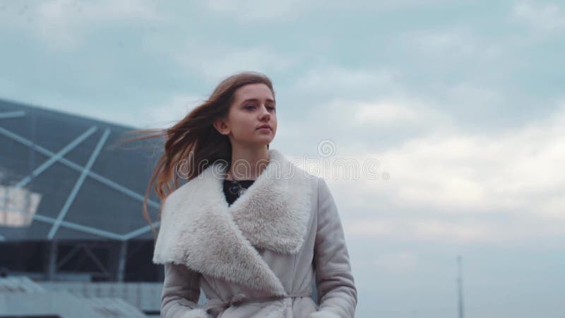 Muchacha europea joven atractiva que se pregunta en el aeropuerto en una capa caliente Muchacha hermosa Tiempo ventoso, juegos de