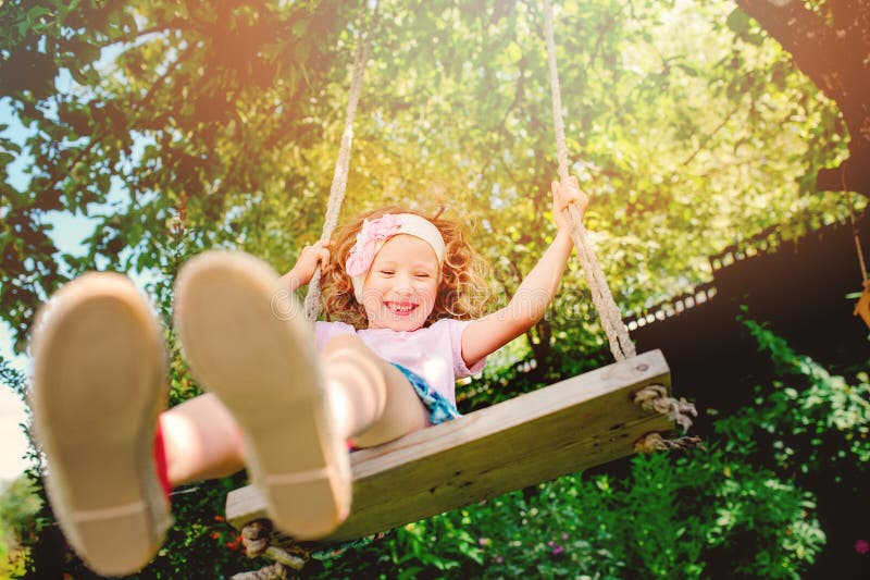 Muchacha feliz del niño en el oscilación en jardín soleado del verano fotos de archivo libres de regalías Muchacha feliz del niño en el oscilación en jardín soleado del verano fotos de archivo libres de regalías