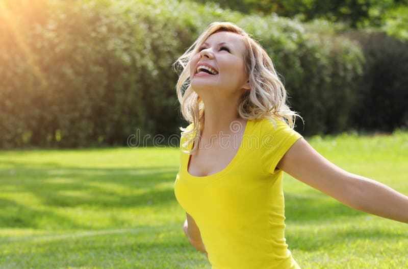 Muchacha feliz que disfruta de la naturaleza en hierba verde.  Mujer joven hermosa que sonríe con los brazos extendidos