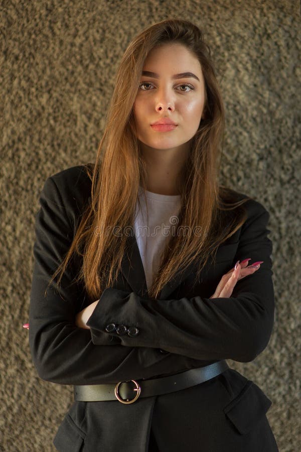 Muchacha hermosa con el pelo largo marrón en una capa negra Señora cerca de la pared gris imagen de archivo Muchacha hermosa con el pelo largo marrón en una capa negra Señora cerca de la pared gris imagen de archivo