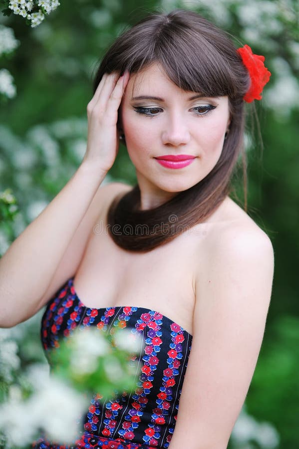 Muchacha hermosa con la flor roja en su cabeza en el jardín de la primavera imagenes de archivo Muchacha hermosa con la flor roja en su cabeza en el jardín de la primavera imagenes de archivo