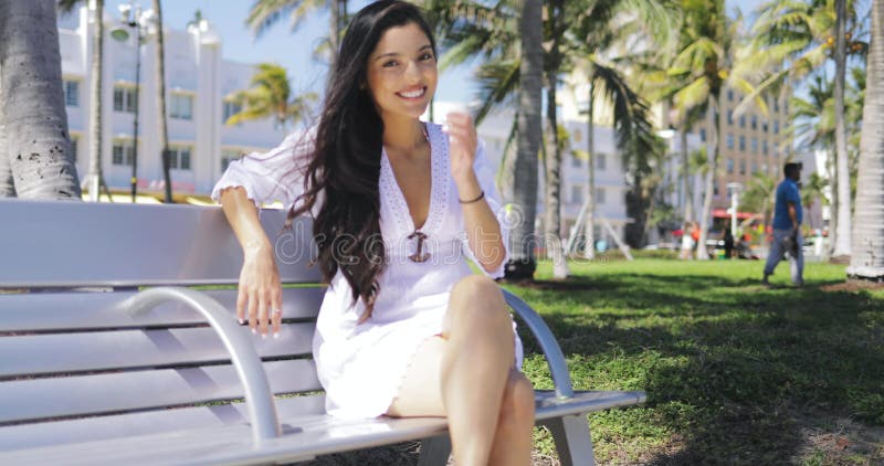 Muchacha hermosa en el vestido blanco en banco en parque