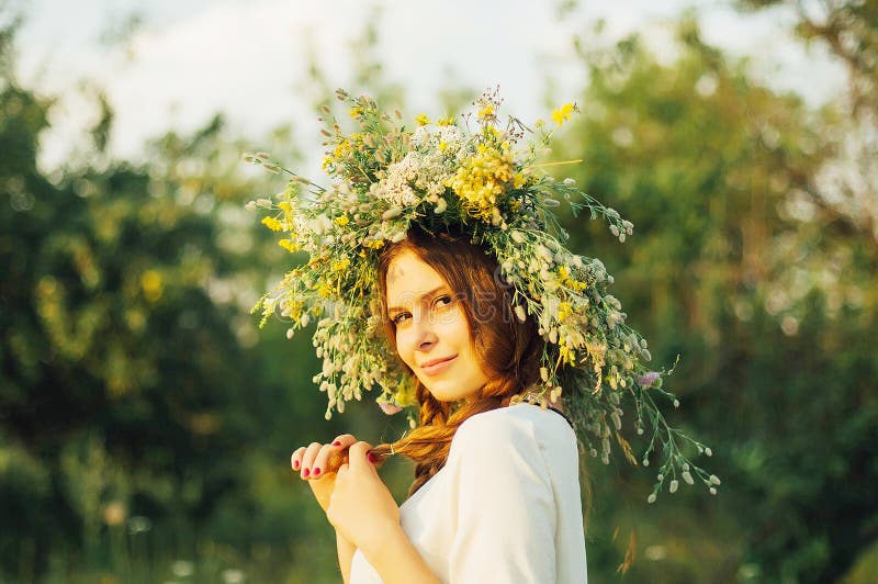 Muchacha hermosa en la guirnalda de flores en prado el día soleado Retrato de la mujer hermosa joven que lleva una guirnalda de f imagen de archivo libre de regalías Muchacha hermosa en la guirnalda de flores en prado el día soleado Retrato de la mujer hermosa joven que lleva una guirnalda de f imagen de archivo libre de regalías