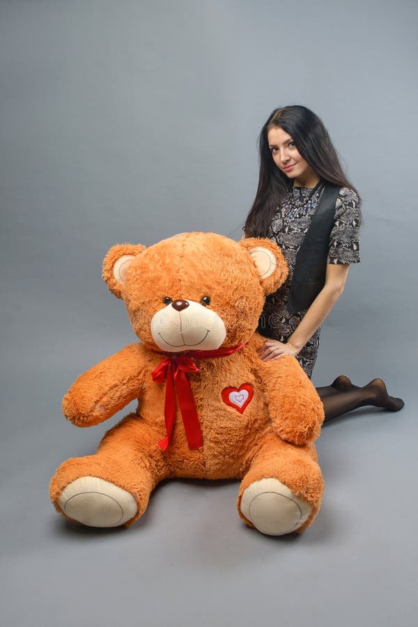 Muchacha hermosa joven con la sonrisa feliz de peluche del juguete suave grande del oso y jugar en fondo gris foto de archivo Muchacha hermosa joven con la sonrisa feliz de peluche del juguete suave grande del oso y jugar en fondo gris foto de archivo