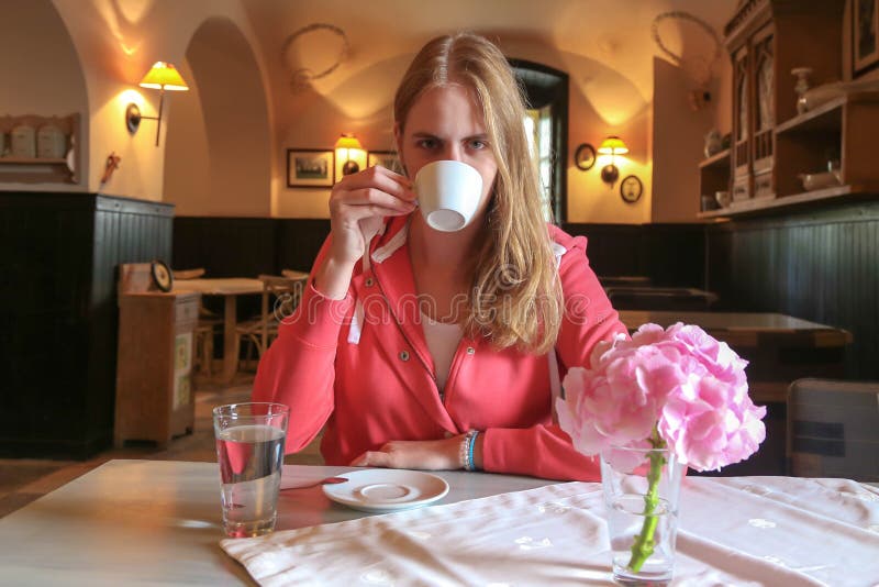 Muchacha hermosa joven que se sienta en un café y un café de consumición imagen de archivo libre de regalías Muchacha hermosa joven que se sienta en un café y un café de consumición imagen de archivo libre de regalías