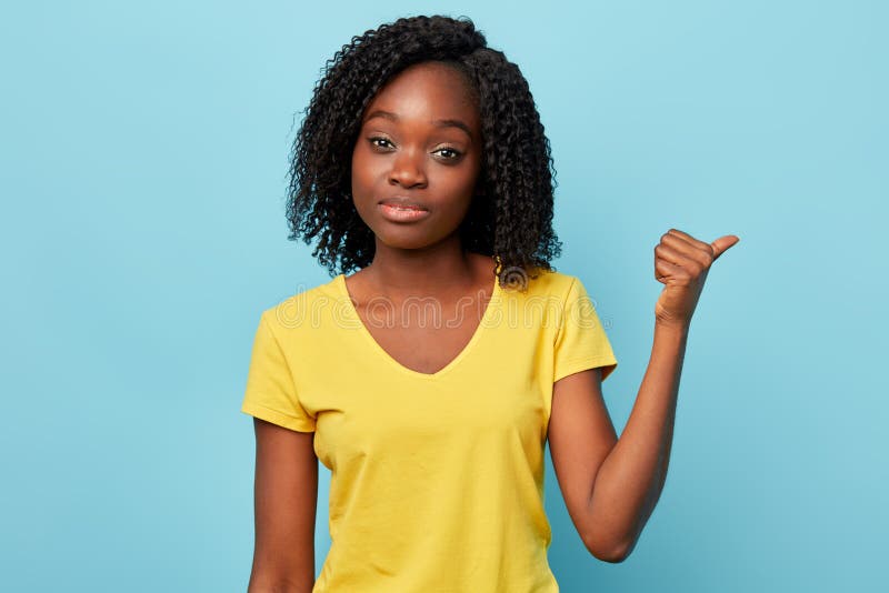 Muchacha impresionante joven que lleva la camiseta elegante que señala al lado con el pulgar para arriba fotos de archivo Muchacha impresionante joven que lleva la camiseta elegante que señala al lado con el pulgar para arriba fotos de archivo
