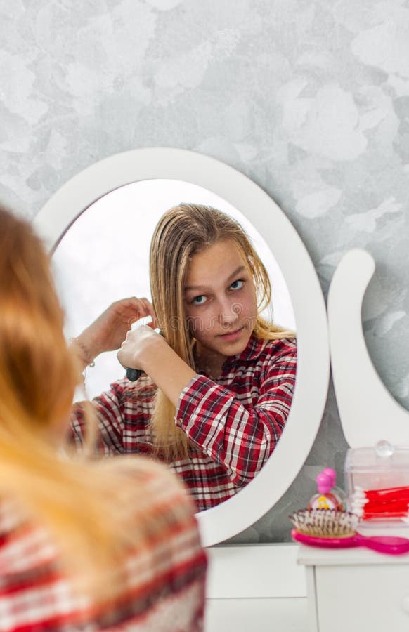 Muchacha joven del adolescente con el pelo largo que se peina el pelo delante de su espejo fotos de archivo Muchacha joven del adolescente con el pelo largo que se peina el pelo delante de su espejo fotos de archivo