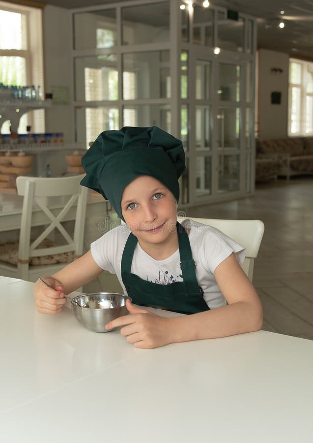 Muchacha joven hermosa del cocinero del cocinero en casquillo verde del cocinero con una cuchara y un cuenco foto de archivo libre de regalías Muchacha joven hermosa del cocinero del cocinero en casquillo verde del cocinero con una cuchara y un cuenco foto de archivo libre de regalías