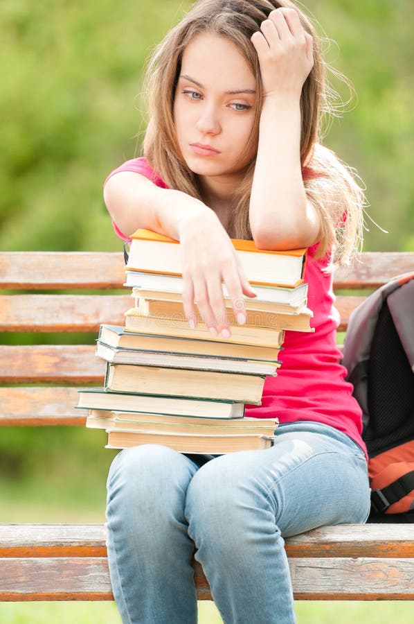 Muchacha joven triste del estudiante que se sienta en banco con los libros fotografía de archivo libre de regalías Muchacha joven triste del estudiante que se sienta en banco con los libros fotografía de archivo libre de regalías
