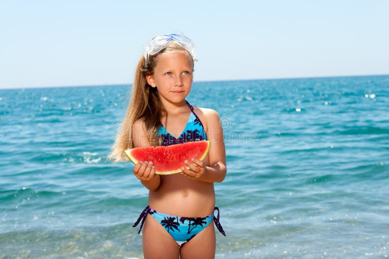 Muchacha linda que come la sandía en la playa.